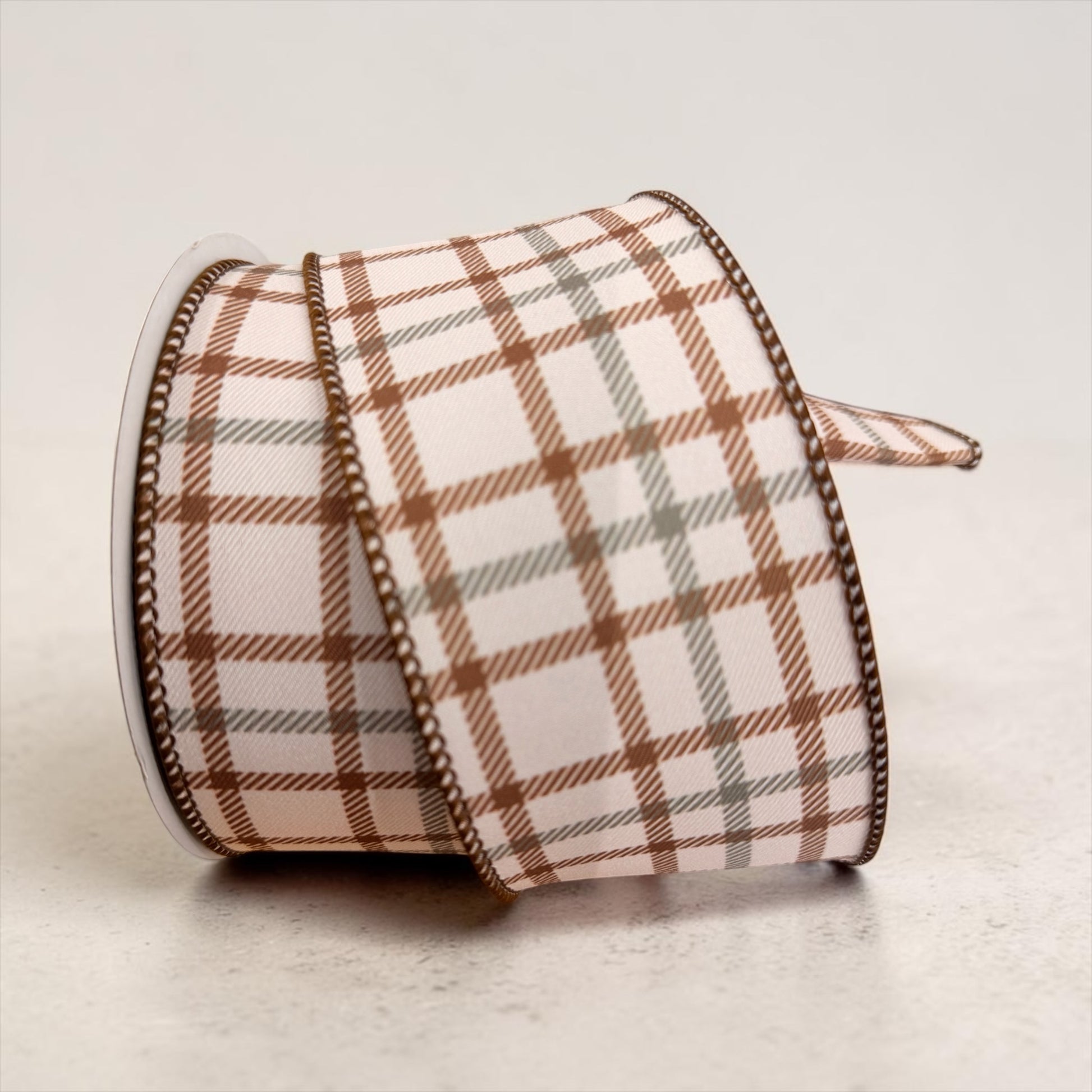 A roll of 2.5-inch wide wired designer ribbon featuring a cream background with a classic plaid pattern in warm brown and soft sage green. The ribbon is shown partially unrolled to display its woven texture and wired edges for shaping decorative bows.