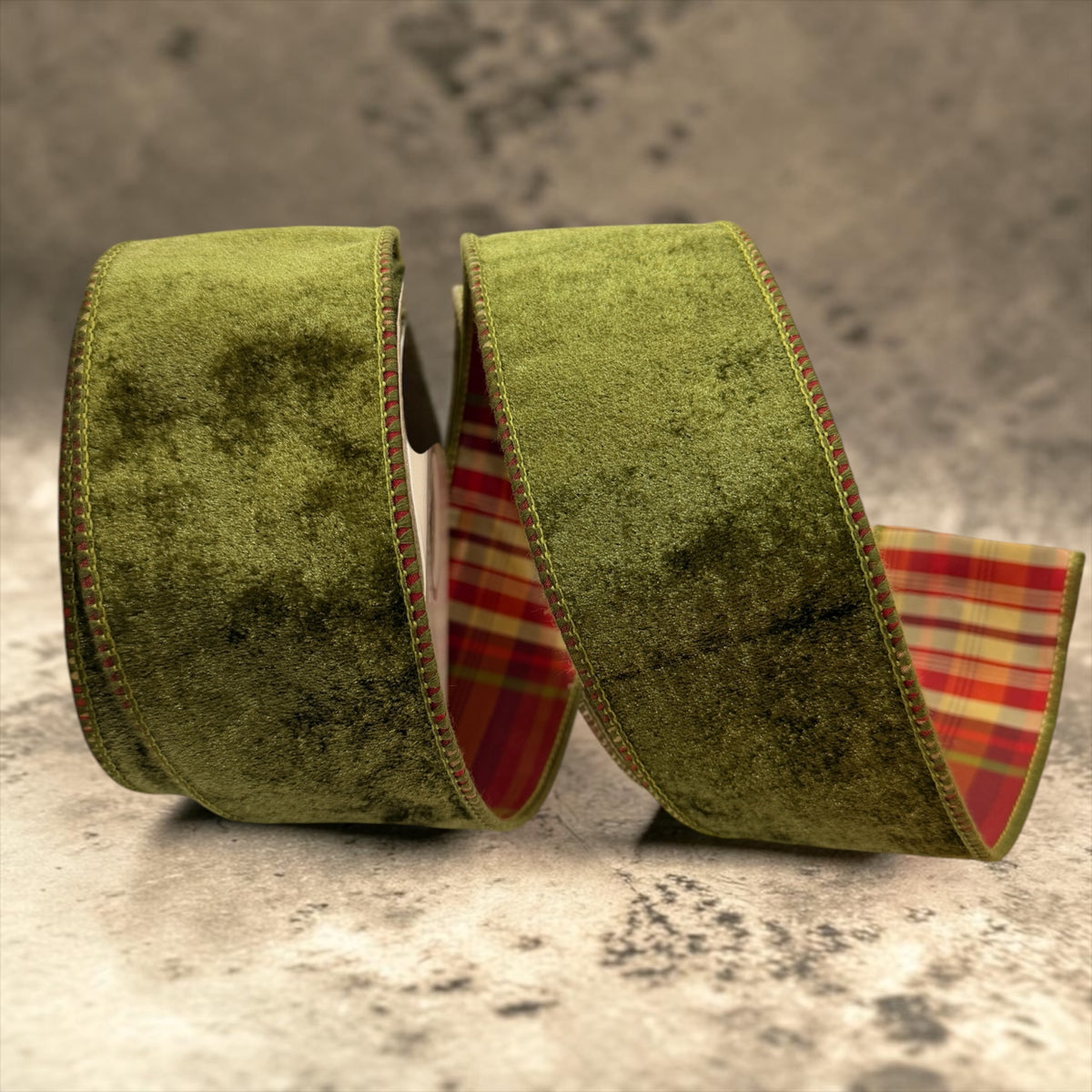 Close-up of deluxe olive green velvet double fused Christmas ribbon with red, gold and green plaid backing and decorative stitched edges, displayed in flowing loops.